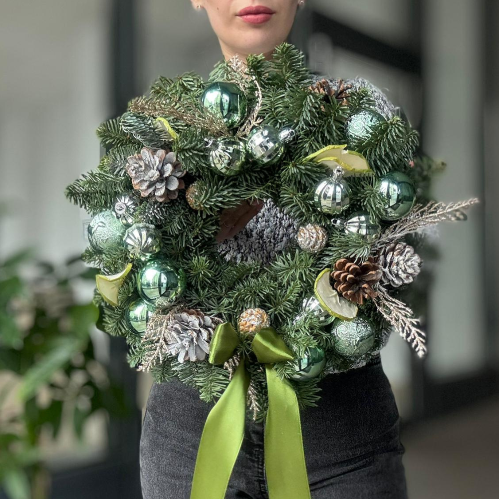 Coroniță „Christmas Blessings” cu conuri și globuri verzi, ținută în mâini